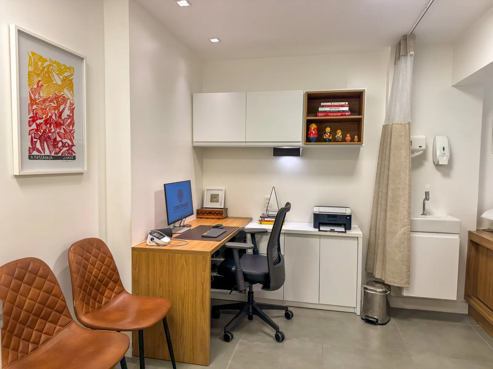 Outro ângulo do consultório, com mesa, cadeiras e estante